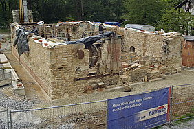 bald ist der Abschluss der Rohbauarbeiten erreicht Fotoaufnahme der beinahe abgeschlossenen Rohbauarbeiten am Erdgeschoss. Lediglich an der Vorderseite fehlt ein Teil der Mauer. Die Oberseite des Mauerwerks wurde mit einer Plane abgedeckt. Im Hintergrund sind ein Teil des Krans sowie eine Baumreihe erkennbar.