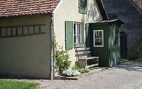 Gelbes Haus mit grünen Fensterläden und einer Bank davor