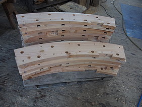 Die 19 Segmente des ersten Radkranzes sind fertig, sie sind auf einer Palette aufgestapelt. Sie sind mit der Verbindung für die Kopfhölzer, sowie mit den Zapfen- und Holznagellöchern versehen.