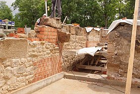 Blickrichtung Südost Fotoaufnahme der letzten Steinreihe auf den unteren Wandabschnitten im Erdgeschoss. Diese besteht überwiegend aus großen Sandsteinquadern. Die Mauer darunter setzt sich aus Bruchsteinen und Ziegeln zusammen. Auf dem vordersten Stein steht ein Arbeiter mit Wasserwaage.