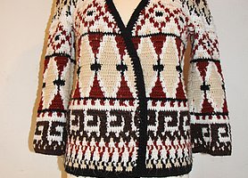 Fotoaufnahme einer Häkeljacke, die dem Torso einer Kleiderpuppe angezogen wurde. Die Häkeljacke ist im Folklorestil bzw. Ethno-Look gehalten und stammt aus den 1970ern. Der Kleiderpuppentorso steht auf einem Tisch aus Holz. 