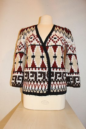 FFM_Objekt_des_Monats_Häkeljacke Fotoaufnahme einer Häkeljacke, die dem Torso einer Kleiderpuppe angezogen wurde. Die Häkeljacke ist im Folklorestil bzw. Ethno-Look gehalten und stammt aus den 1970ern. Der Kleiderpuppentorso steht auf einem Tisch aus Holz.