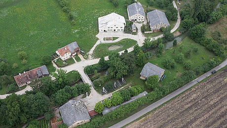 FFM_Altmühlfranken_Luftaufnahme Fotoaufnahme eines Luftbildes der Baugruppe Süd. Das Bild wurde von Süden aus aufgenommen. Die einzelnen Gebäude sind durch Wege miteinander verbunden. Umliegend befinden sich Felder, Wiesen und Bäume.