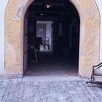 FFM_West_Gaststaette_Kommunbrauhaus_Eingang Fotoaufnahme des Haupteingangs vom Gasthaus aus Mühlhausen bzw. vom Wirtshaus am Kommunbrauhaus am aktuellen Standort. Die zweiflügelige Holztür ist nach innen geöffnet, darüber steht „JS 72“. Der Boden vor dem Gebäude ist gepflastert.