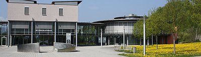 Bezirksrathaus bestehend aus mehreren aneinandergebauten unterschiedlichen Gebäuden; daneben Blumenwiese