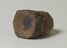 Der Stein ist auf der einen Seite rund, auf der anderen flach. Auf der flachen Seite sind Farbreste. Mit dem Stein wurden Farbpigmente gerieben.