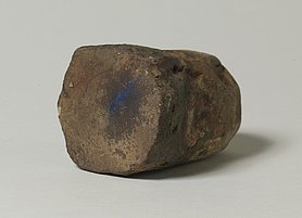 Der Stein ist auf der einen Seite rund, auf der anderen flach. Auf der flachen Seite sind Farbreste. Mit dem Stein wurden Farbpigmente gerieben.