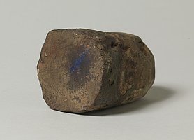 Der Stein ist auf der einen Seite rund, auf der anderen flach. Auf der flachen Seite sind Farbreste. Mit dem Stein wurden Farbpigmente gerieben.