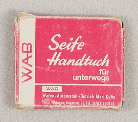 Die Schachtel ist rechteckig. Sie ist aus Pappe. Sie ist rot bedruckt. Die Schrift ist weiß. in der Schachtel steckt ein Tuch.