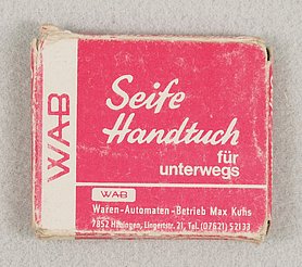 Die Schachtel ist rechteckig. Sie ist aus Pappe. Sie ist rot bedruckt. Die Schrift ist weiß. in der Schachtel steckt ein Tuch.