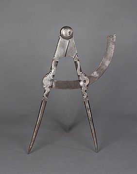 Der Zirkel ist aus Eisen. Er hat zwei Schenkel. Beide sind vorne spitz. Sie sind miteinander verbunden. Sie können an einem Bogen entlang gedreht werden. Die Schenkel sind verziert.
