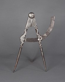 Der Zirkel ist aus Eisen. Er hat zwei Schenkel. Beide sind vorne spitz. Sie sind miteinander verbunden. Sie können an einem Bogen entlang gedreht werden. Die Schenkel sind verziert.