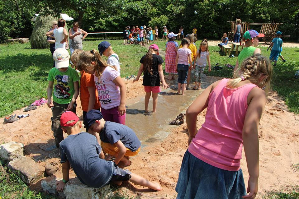 FFM_Eroeffnung_Erlebnisplatz_Wasserrinne Fotoaufnahme der Wasserrinne auf dem Erlebnisplatz in der Baugruppe Süd. Im Vordergrund befindet sich der Sandkasten, durch den die meterbreite Wasserrinne führt. Zahlreiche Kinder laufen barfüßig hindurch. Dahinter sind weitere Stationen des Platzes mit noch mehr Kindern erkennbar.