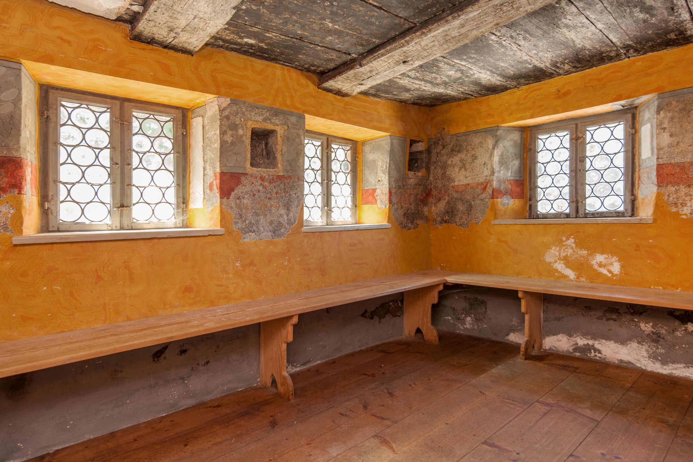 Die Stube hat gelbe Wände. In ihr ist eine Bank. Die Decke ist aus Holz.