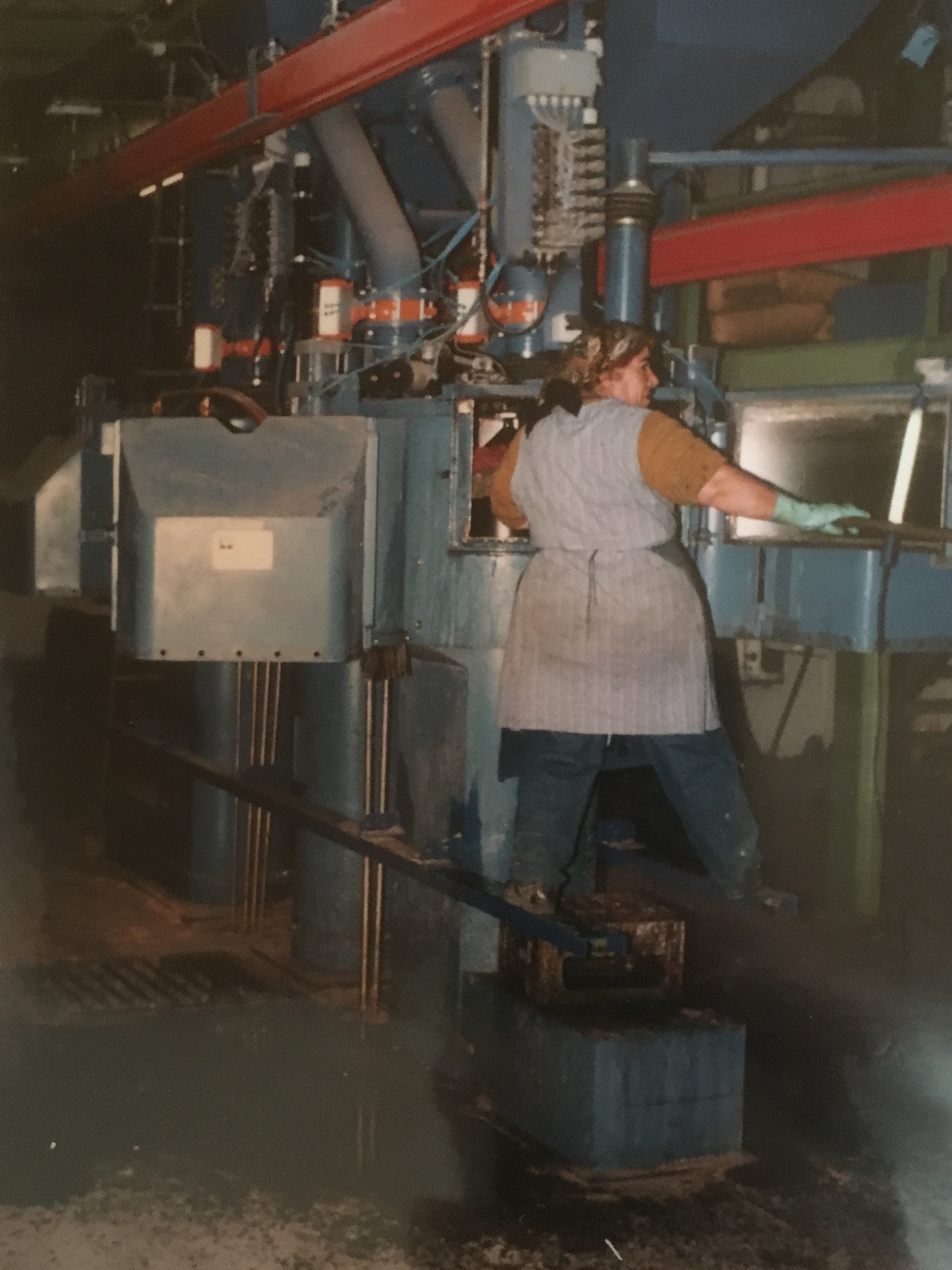 Eine Frau arbeitet an einer Maschine. Sie ist in einer Gießerei. Die Frau stammt aus der Türkei. Sie wohnt und arbeitet in Deutschland.