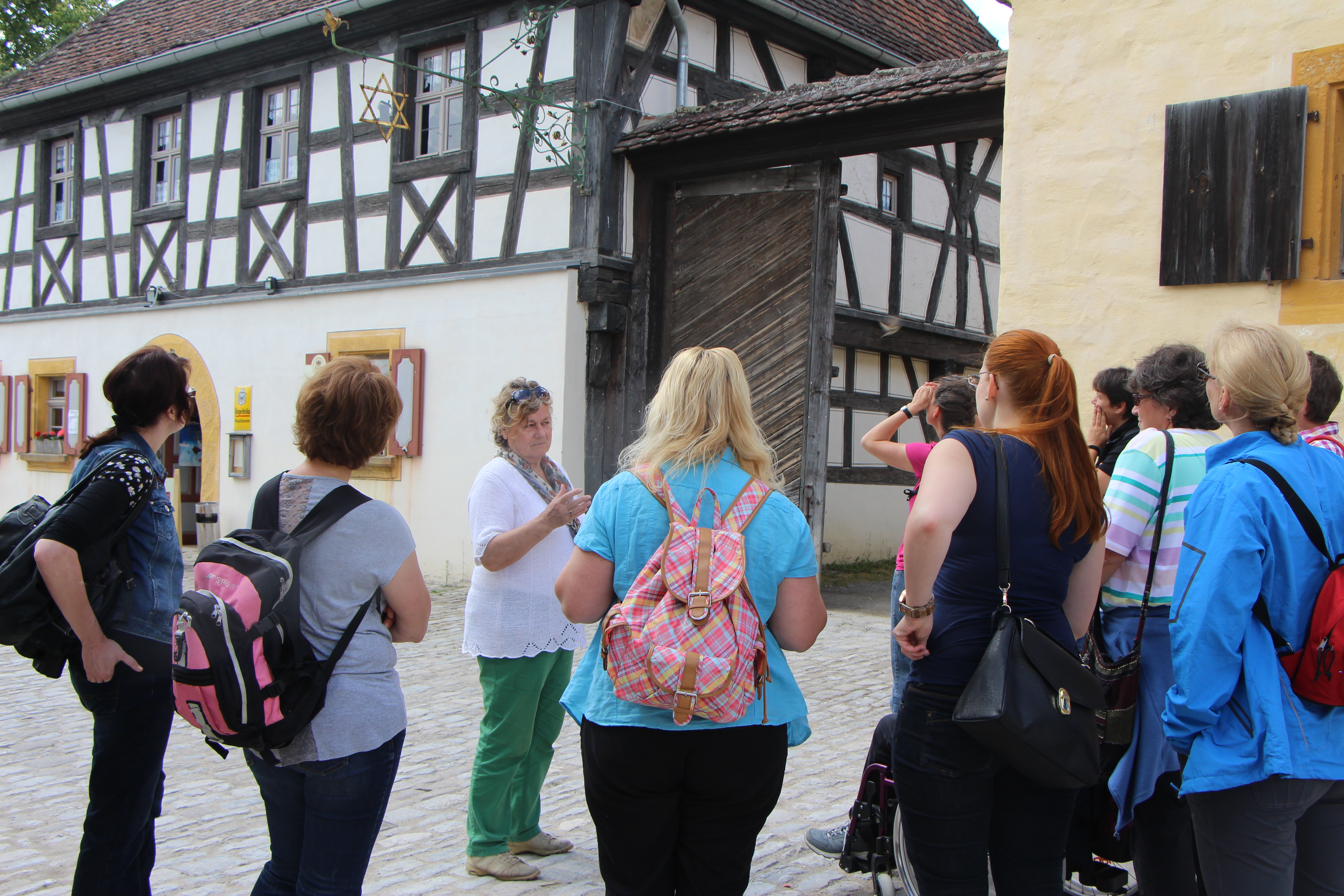Fotoaufnahme einer allgemeinen Überblicksführung für Erwachsene. Die Gruppe Frauen steht auf dem gepflasterten Hof vor dem Wirtshaus am Kommunbrauhaus. Sie blicken zu dem Fachwerkhaus empor. An der Fassade hängt ein Brauerstern mit Maßkrug in der Mitte. 